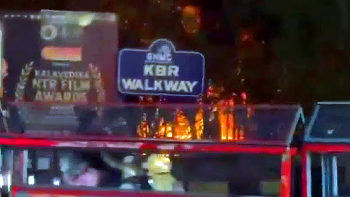 Fire flames seen near the KBR Walkway sign at KBR Park in Hyderabad as a city bus passes by at night.
